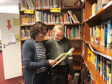 Gesina Kegel schaut gemeinsam mit Schülerin in Buch - Ehrenamt in der Schulbibliothek